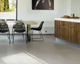 Un salon moderne avec un carrelage pièce de vie tendance, une table en bois, des chaises noires design et un îlot de cuisine en bois veiné.