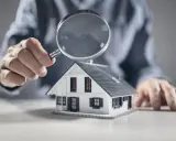 Une main examine une maquette de maison avec une loupe, symbolisant l'analyse pour un crédit construction maison.