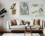Un salon moderne avec un canapé gris, des coussins texturés et un mur de cadre orné de trois tableaux : art abstrait, oiseaux et paons dans un jardin.