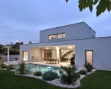 Vue arrière d'une maison moderne avec piscine illuminée, terrasse et jardin paysager. Un exemple de plan maison de luxe.