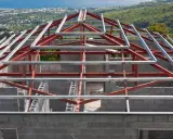 Structure métallique d'une maison en construction, avec des poutres rouges et grises. Un inconvénient potentiel de ce type de maison est la nécessité d'une isolation thermique soignée.