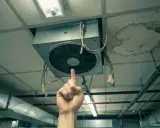 Une main pointe un VMC bruyant au plafond, à côté d'une tache d'humidité.