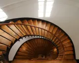 Vue plongeante d'un escalier en colimaçon en bois, parfait pour une rénovation cage escalier immeuble. La lumière naturelle illumine les marches.