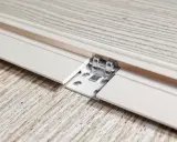 Détail d'une lame PVC qui se soulève, révélant une fixation métallique et des vis sur un parquet imitation bois.