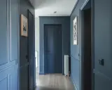 Peinture d'un couloir aux tons bleus profonds, avec des portes assorties et des cadres de portes ornés. Des tableaux discrets ornent les murs.