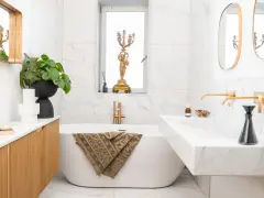 Élégante salle de bain moderne petite avec baignoire îlot, lavabo en marbre, robinetterie dorée et un bougeoir ancien.