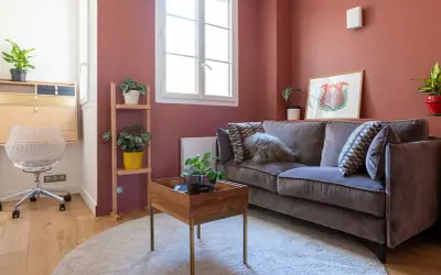 Chambre d'amis confortable avec un canapé convertible (clic clac) en velours gris, des plantes vertes et un bureau mural.