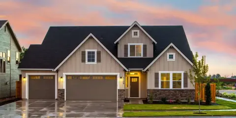 Belle maison prête à finir, prix attractif. Façade beige, toit noir, garage double, jardin verdoyant sous un ciel pastel.