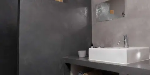 Salle de bain moderne avec murs en béton ciré. Une douche sans joint, un lavabo rectangulaire et des serviettes pliées créent une ambiance épurée.