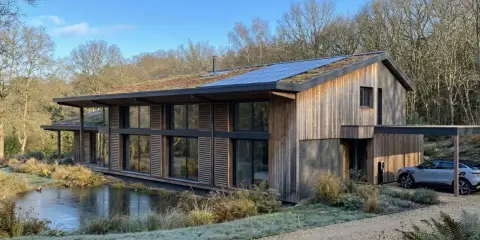 Une maison écologique moderne avec un toit végétalisé et des panneaux solaires, nichée près d'un étang gelé.