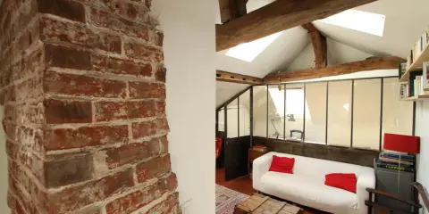 Aménagement combles idées : un salon cosy sous les toits avec murs en briques apparentes, poutres en bois et canapé blanc.