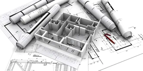 Maquette 3D d'une maison familiale sur des plans d'architecte, avec des rouleaux de plans et des stylos rouges.