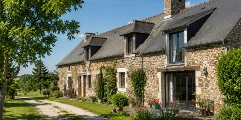 Longère moderne en pierre avec un chemin de gravier menant à l'entrée. Un jardin fleuri borde la façade.