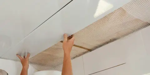 Mains installant des panneaux blancs pour refaire un plafond, avec un treillis visible en dessous.