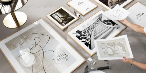 Un mur de cadre couloir prend forme avec des œuvres abstraites et photographiques. Un marteau et des clous sont prêts pour l'accrochage.