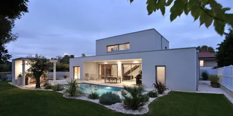 Vue arrière d'une maison moderne avec piscine illuminée, terrasse et jardin paysager. Un exemple de plan maison de luxe.
