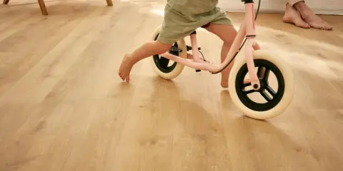 Un enfant apprend à faire du vélo d'équilibre sur un sol de salle de jeux en bois clair.