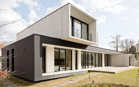 Maison moderne avec façade en béton et bardage sombre, grande baie vitrée et terrasse en bois.