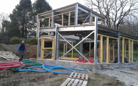 Chantier d'une maison ossature métallique, structure en acier et bois, avec des tuyaux colorés au sol.