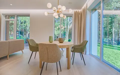 Éclairage salle à manger sans plafonnier : suspension moderne au-dessus d'une table ronde, entourée de chaises vertes. Lumière naturelle abondante des grandes fenêtres.