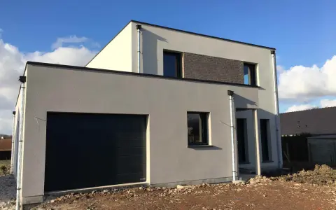 Maison moderne avec garage intégré. La couleur façade maison est un gris clair, contrastant avec des touches de blanc cassé et un bandeau de briques sombres.