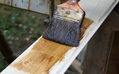 Application d'une lasure bois pour un avant-après visible. Le pinceau dépose une teinte chaude sur le bois brut.