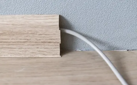 Une plinthe en bois imite le bois et cache un fil électrique. Astuce pour comment cacher des fils électriques.