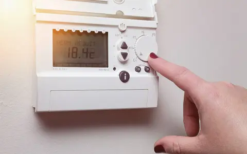 Main d'une femme ajustant un cee thermostat connecté affichant 18.4°C.