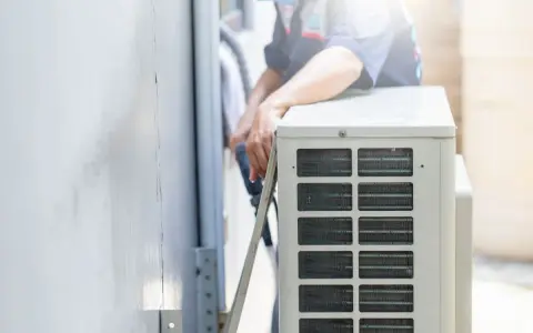 Un technicien s'occupe de recharger la clim de la maison. Il manipule des tuyaux près de l'unité extérieure.