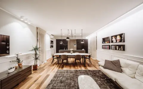 Un grand salon moderne avec un canapé blanc, une table à manger ovale et une cuisine intégrée. La taille du salon est optimisée pour le confort.