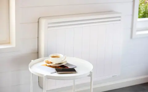 Un radiateur blanc moderne, idéal pour le chauffage maison neuve, avec une tasse de café et des magazines sur une table d'appoint.