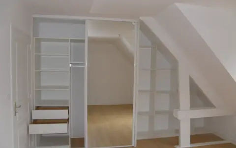 Aménagement astucieux pour faire un dressing sous pente. Étagères et tiroirs blancs s'intègrent parfaitement à l'espace mansardé.