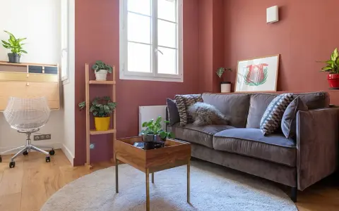 Chambre d'amis confortable avec un canapé convertible (clic clac) en velours gris, des plantes vertes et un bureau mural.