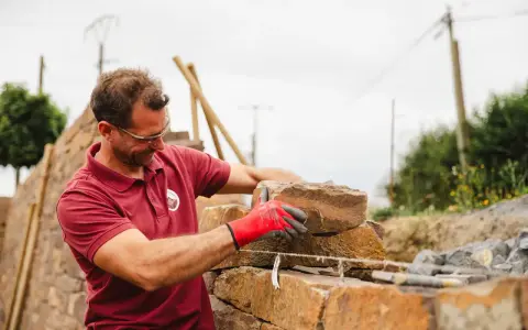 Un maçon, ganté de rouge, pose une pierre pour construire un mur en Corse.