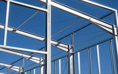 Structure métallique d'un bâtiment en construction, avec des poutres et des poteaux d'acier sous un ciel bleu clair.