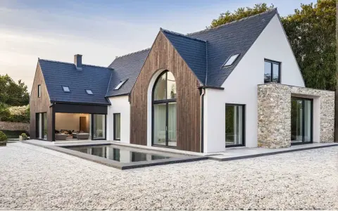 Une maison neuve en pierre et bois, avec une piscine rectangulaire devant.