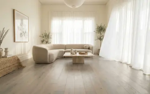Un salon lumineux avec un canapé incurvé beige, une table basse en pierre et un sol en bois gris clair. Le beige et le blanc s'accordent parfaitement avec le gris clair.
