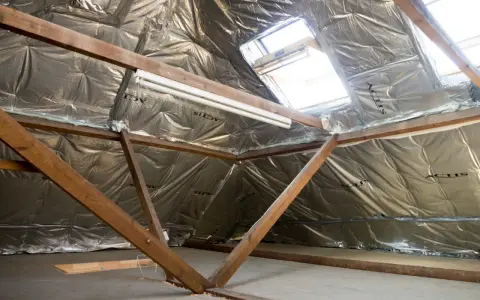 Isolation argentée sous les combles, avec poutres en bois et fenêtres de toit. Un système VMC sans comble est en cours d'installation.