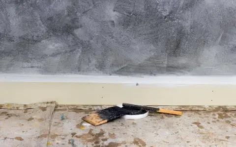 Outils pour enduire un mur abîmé : spatules et pot de mastic sur une bâche de protection au sol.