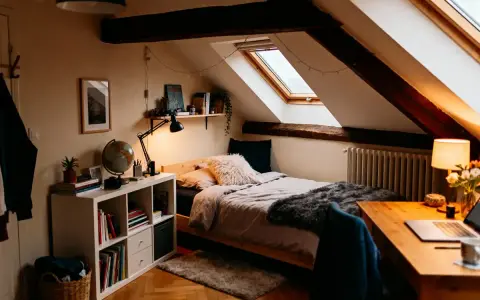 Chambre sous comble très bas, avec lit douillet, bureau et étagères. Lumière chaleureuse et poutres apparentes.