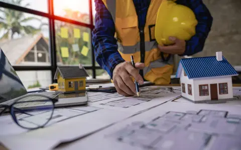 Un architecte examine des plans pour une maison ancienne, évaluant le DPE. Maquettes de maisons sur la table.