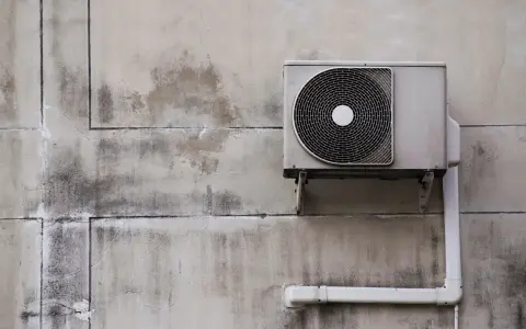 Unité extérieure d'une pompe à chaleur fixée sur un mur en béton. L'isolation est visible sur le tuyau blanc.