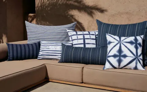 Plusieurs coussins bleus et blancs, à rayures et motifs tie-dye, sont disposés sur un canapé marron. Idée pour comment mettre un plaid sur un canapé.