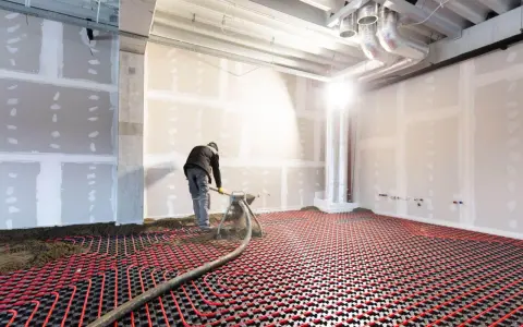 Un ouvrier installe un système de chauffage au sol hydraulique. Des tuyaux rouges serpentent sur une grille noire, prêts à diffuser une chaleur douce.