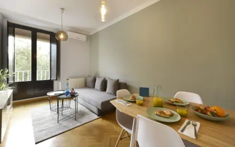 Un salon salle à manger de 20m2 prêt pour le petit-déjeuner, avec un canapé confortable, une table en bois garnie de croissants et de jus d'orange, et une grande fenêtre lumineuse.