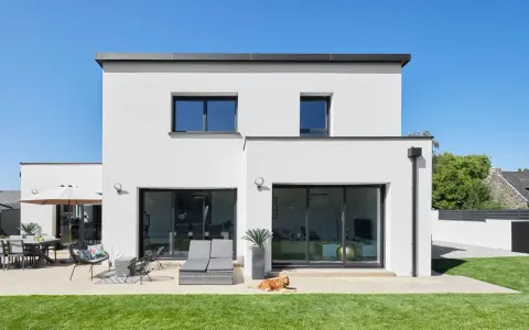 Maison moderne avec jardin, terrasse et chien. La ptz construction maison est visible sous un ciel bleu éclatant.