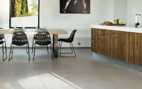 Un salon moderne avec un carrelage pièce de vie tendance, une table en bois, des chaises noires design et un îlot de cuisine en bois veiné.
