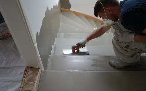 Un ouvrier, masqué et ganté, applique un enduit sur les marches d'un escalier en cours de restauration.