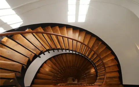 Vue plongeante d'un escalier en colimaçon en bois, parfait pour une rénovation cage escalier immeuble. La lumière naturelle illumine les marches.