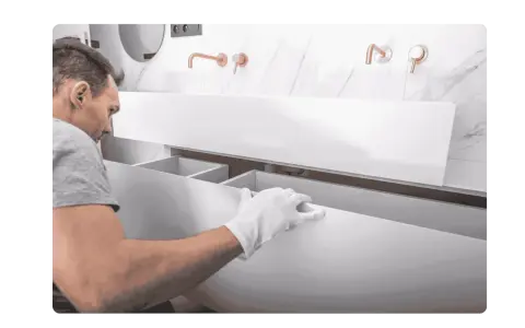 Un homme en gants blancs installe un meuble de salle de bain suspendu. Il s'assure de bien fixer meuble lourd sur placo pour une installation solide.